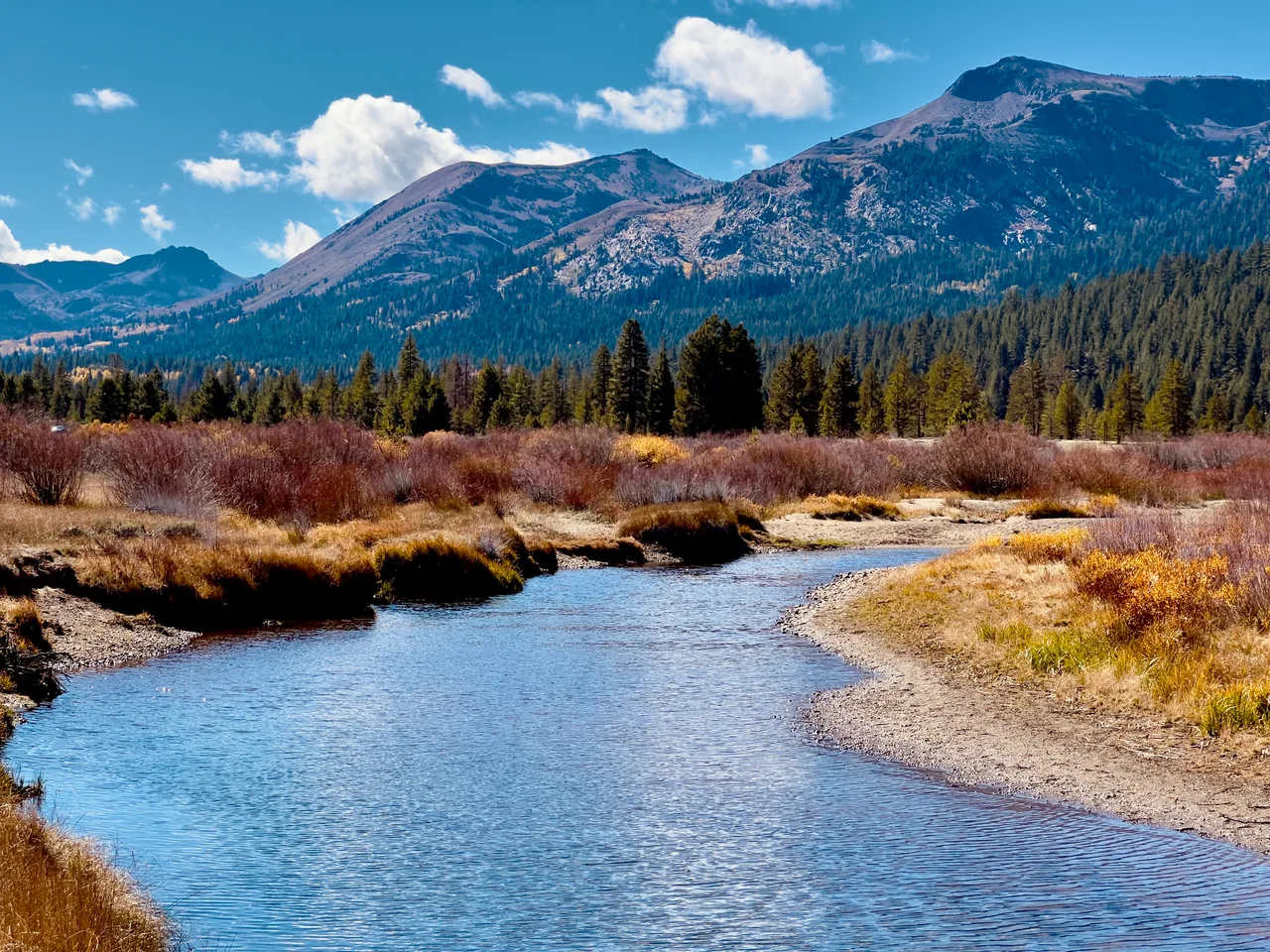 A winding creek bordered by golden vegetation beneath rugged mountains
