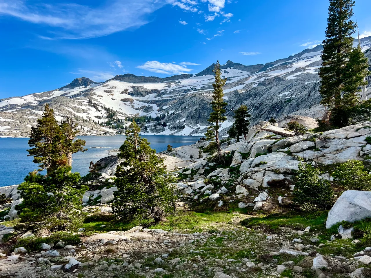 Pines and pale granite beside a lake below snowy mountain slopes