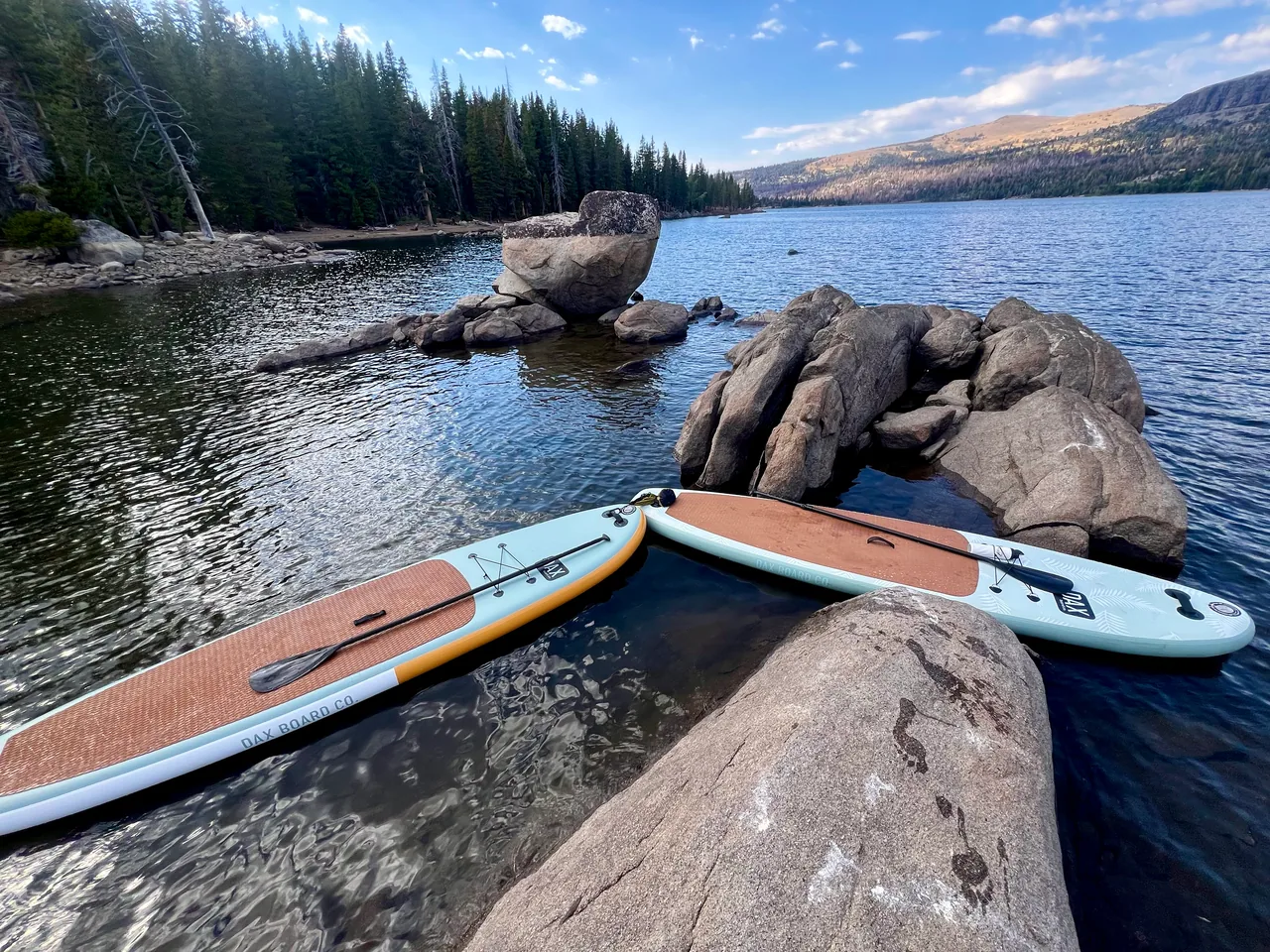 Two paddleboards resting on granite rocks beside a mountain lake
