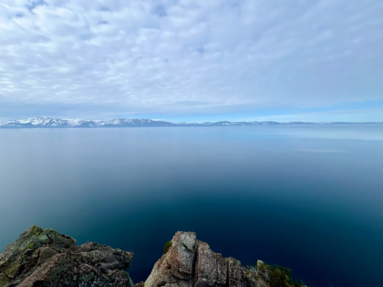 Rocks at the edge of still blue water under a textured sky