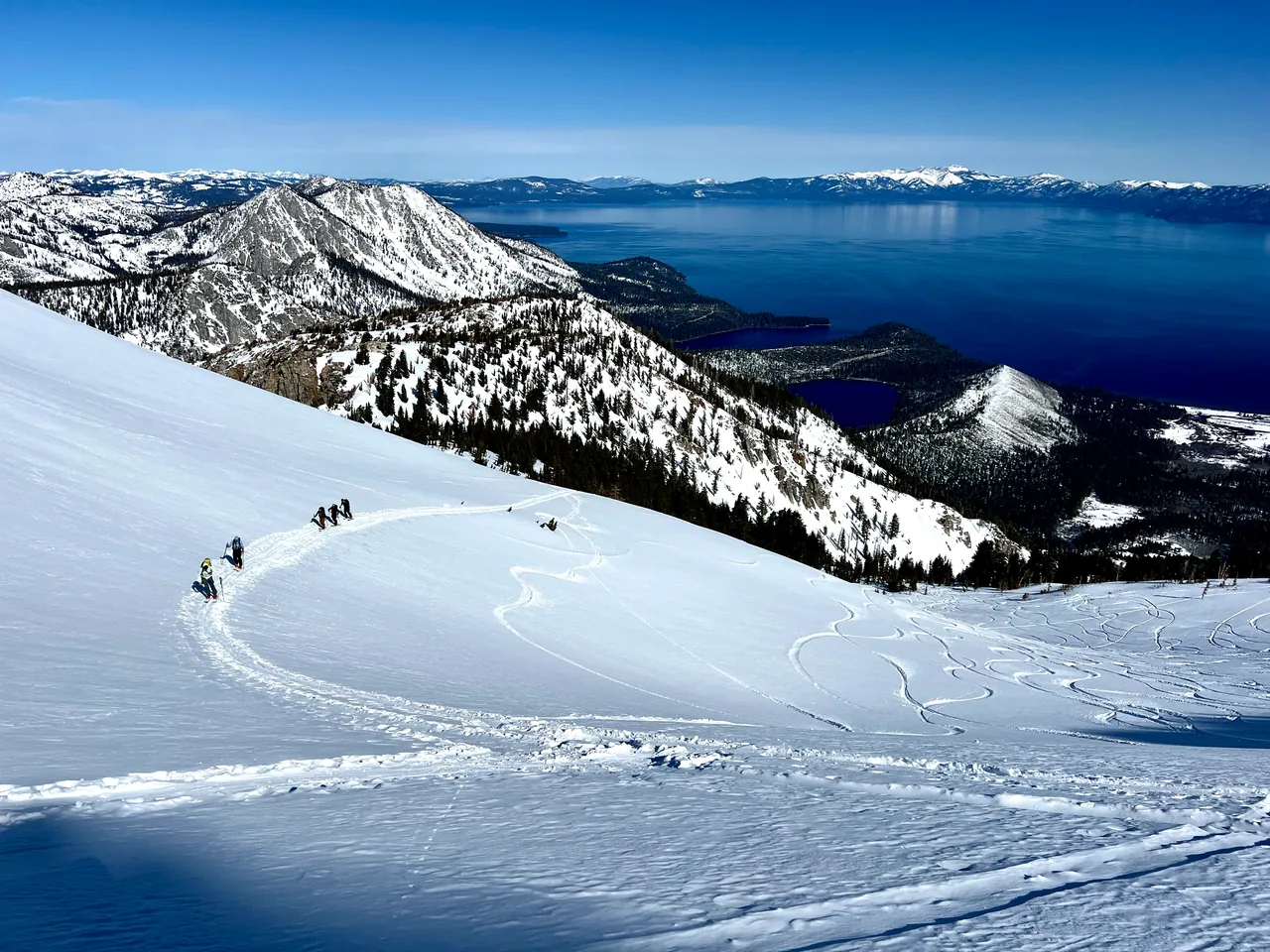 A snowy mountainside descending toward deep blue Lake Tahoe