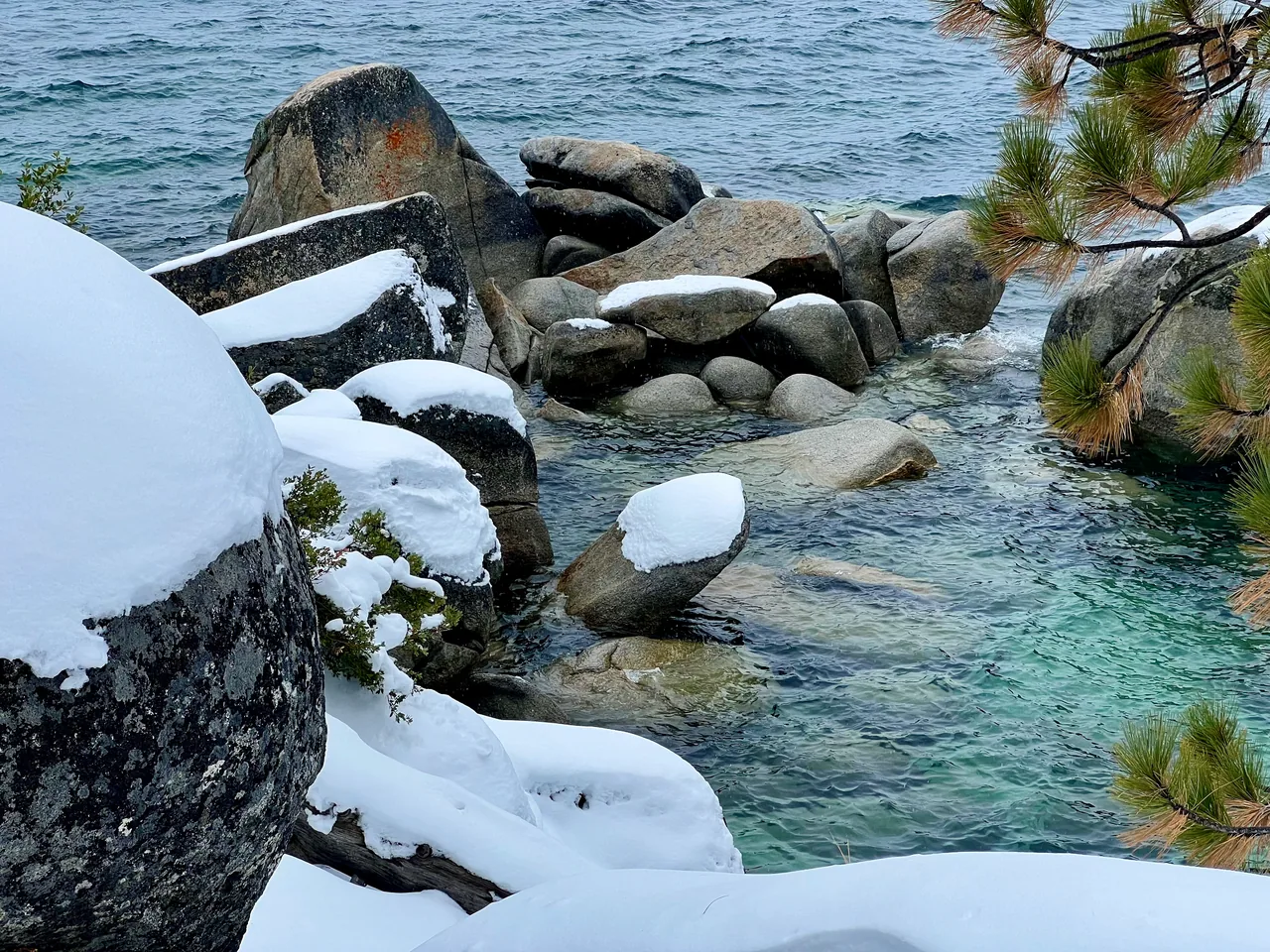 Snow-covered granite boulders beside transparent turquoise water