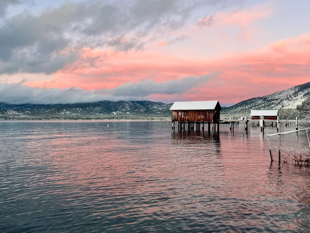 A snow-covered boathouse and pier beneath a pink winter sky